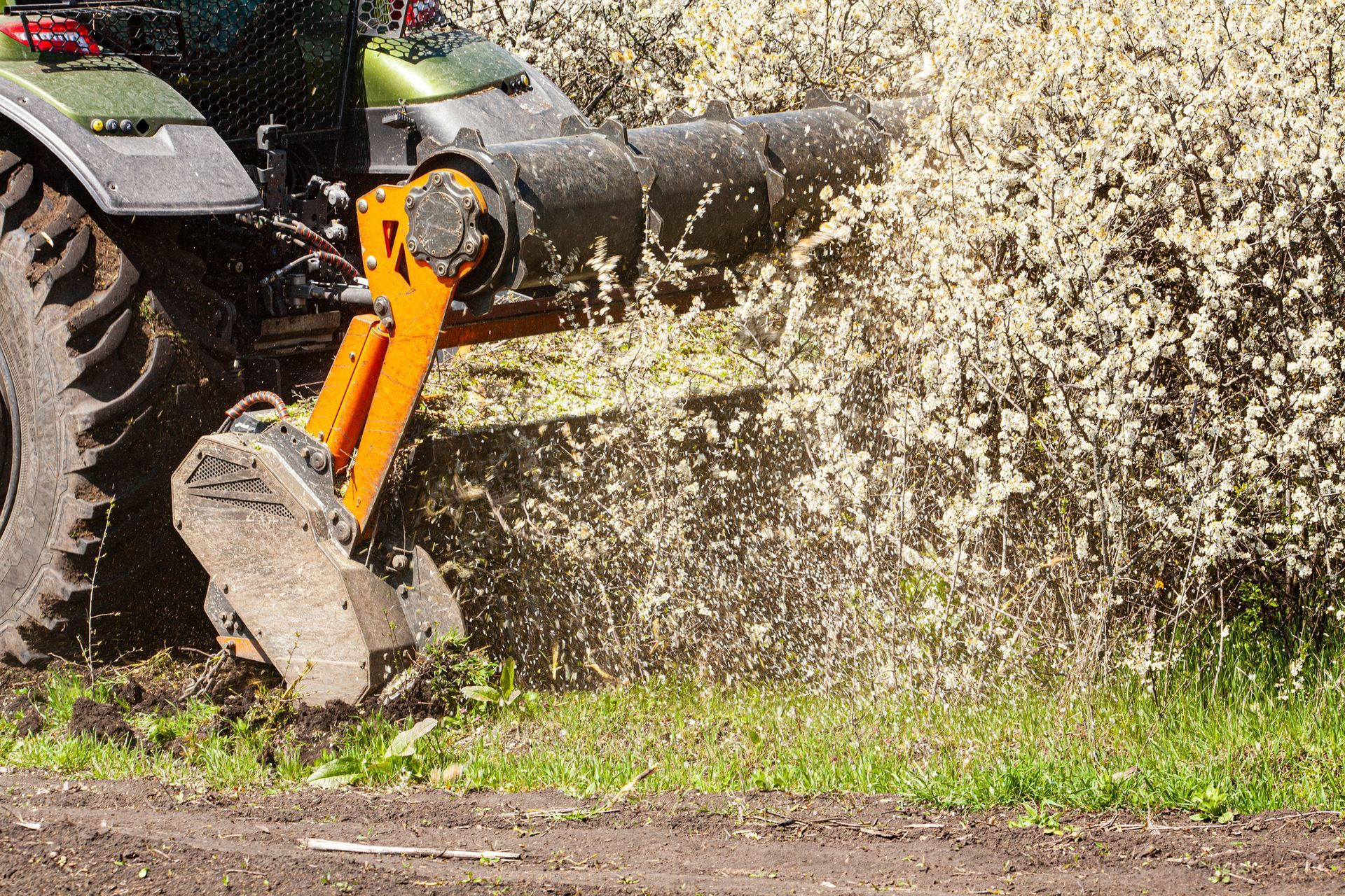 A tractor with an orange arm mulches brush on the edge of a field.