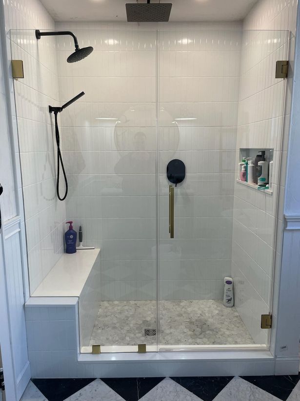 A bathroom with a walk in shower with a glass door and a bench.