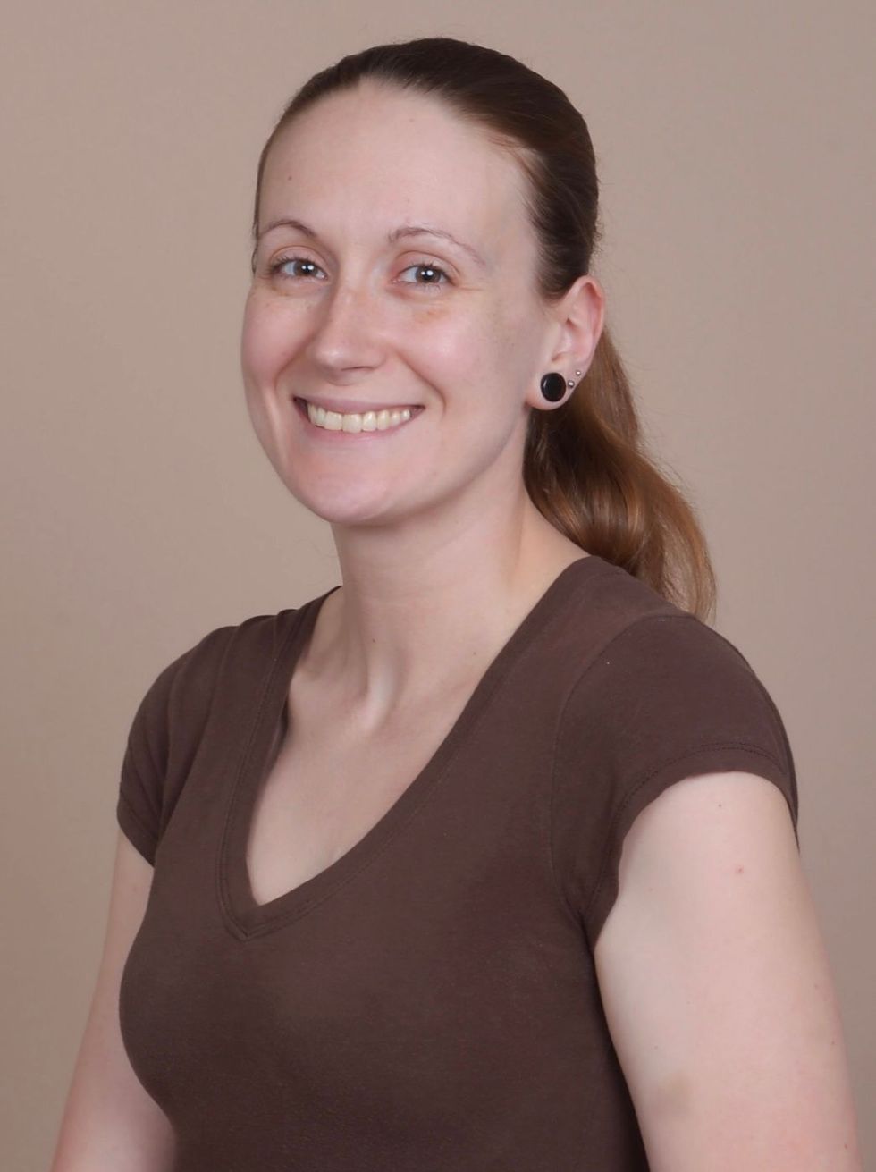 A woman wearing a brown shirt and black earrings smiles for the camera