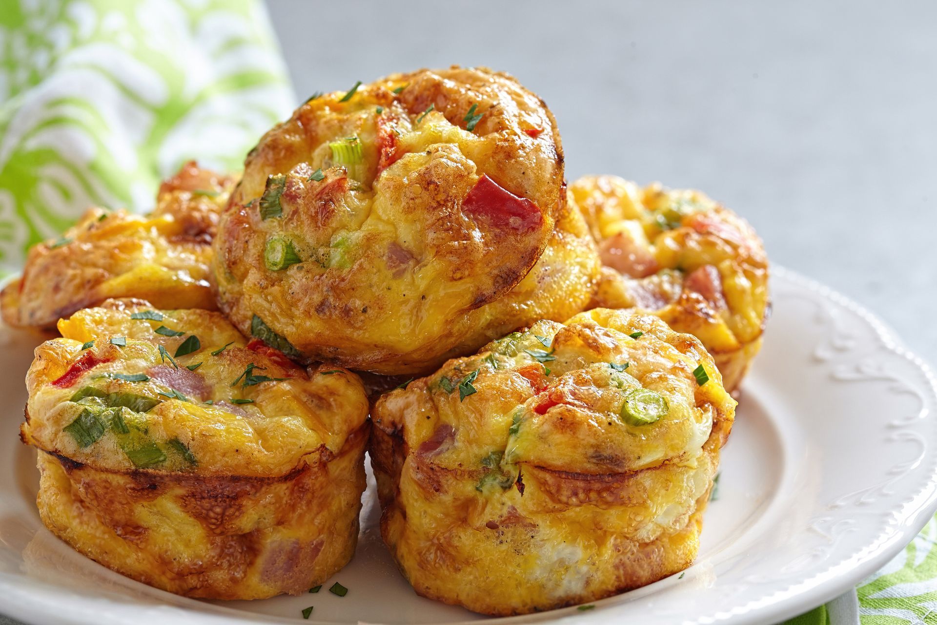 Savory breakfast egg muffins on a white plate, filled with colorful vegetables and ham, close-up shot.