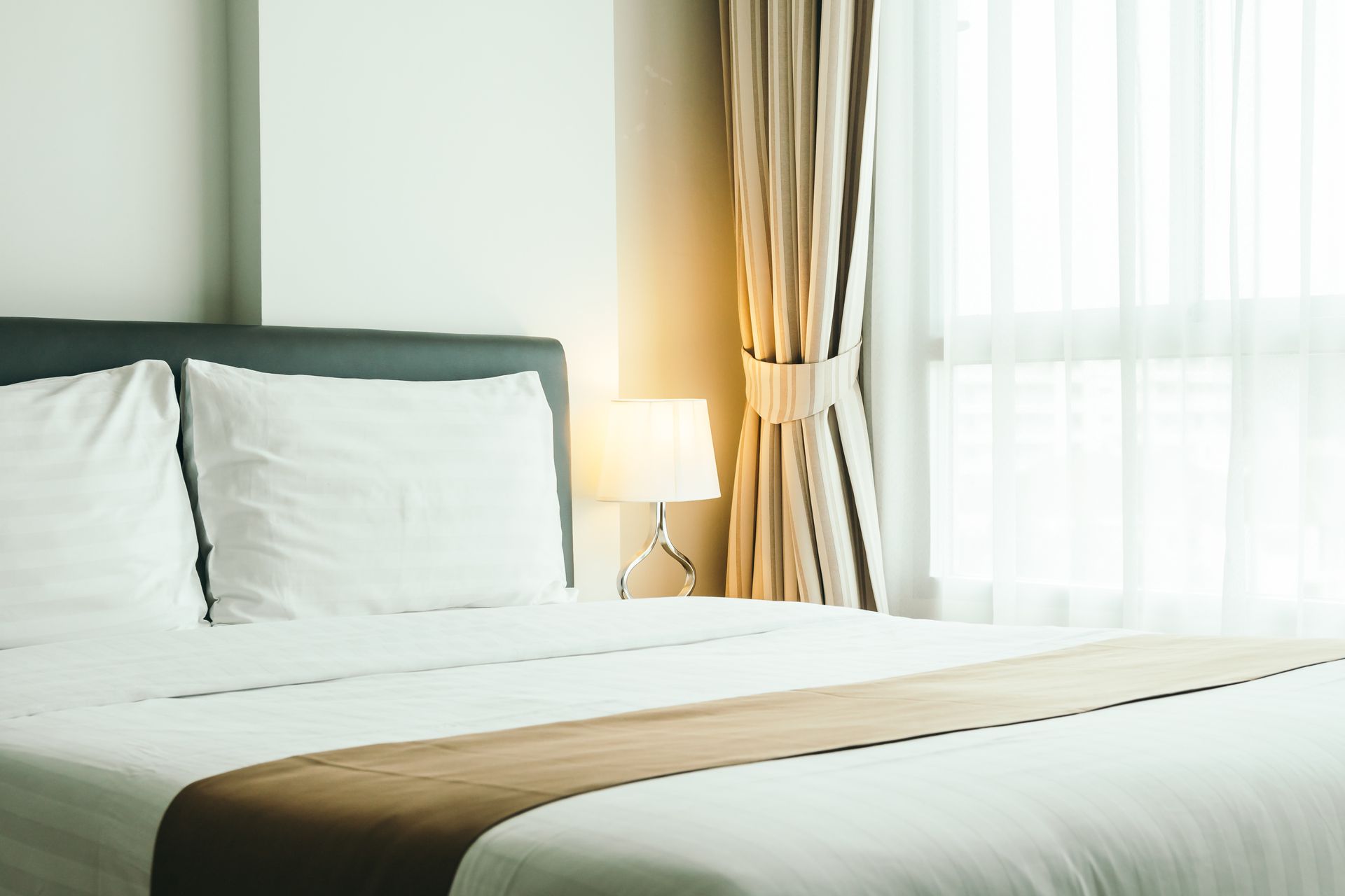A hotel room with a bed , curtains , a lamp and a window.