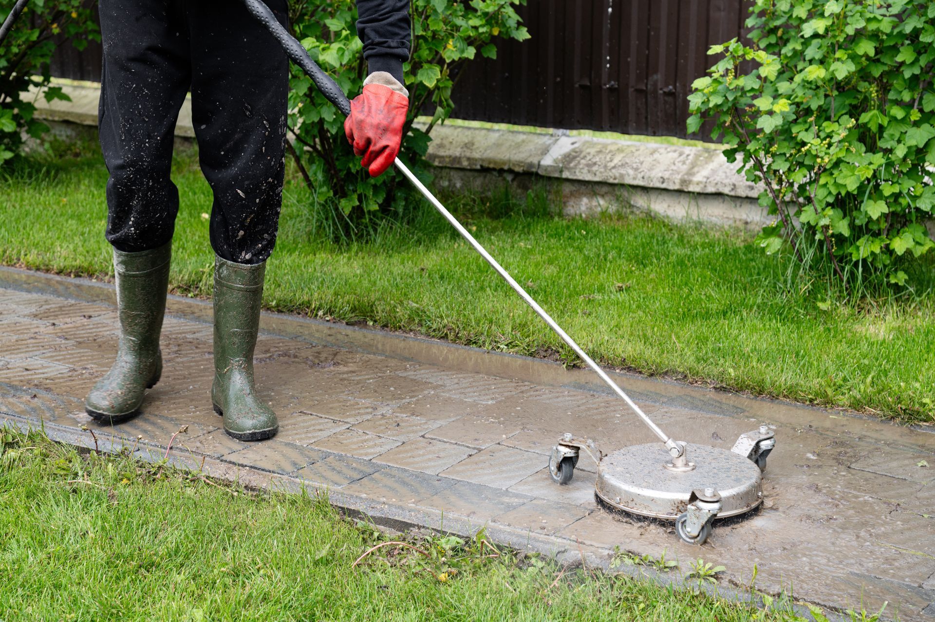 A person is cleaning a sidewalk with a high pressure washer.