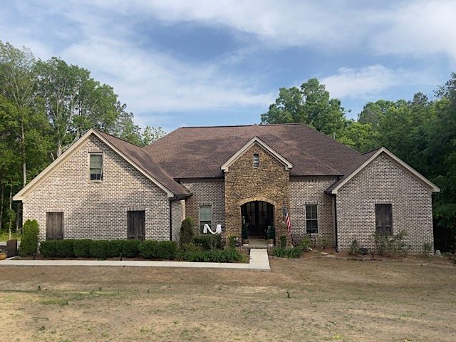 A large brick house with a brown roof is surrounded by trees