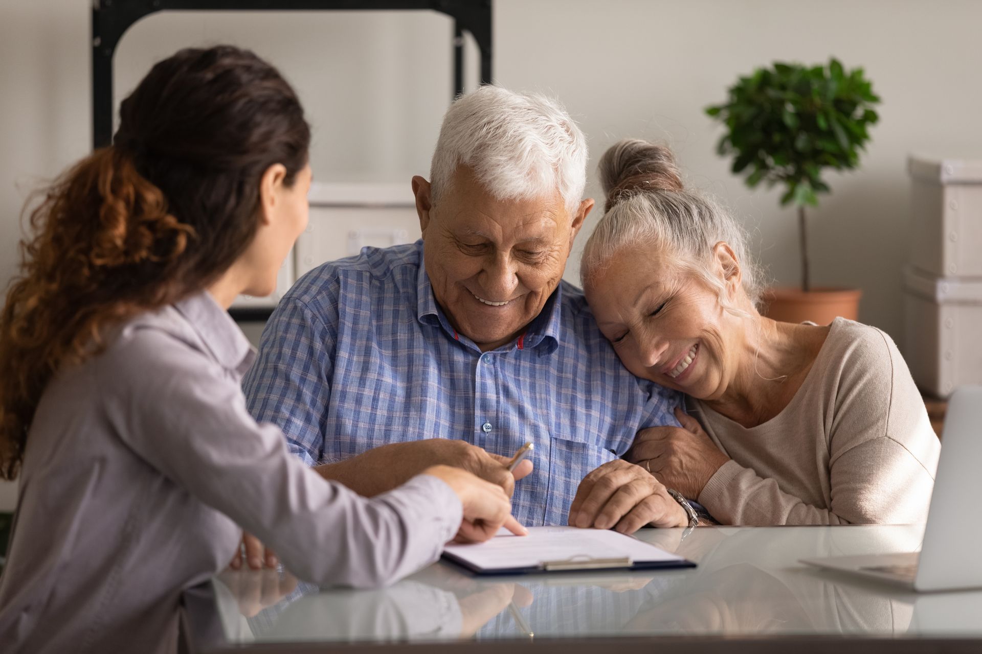 An advisor reviews a retirement plan with an elderly couple in a bright, cozy living room.