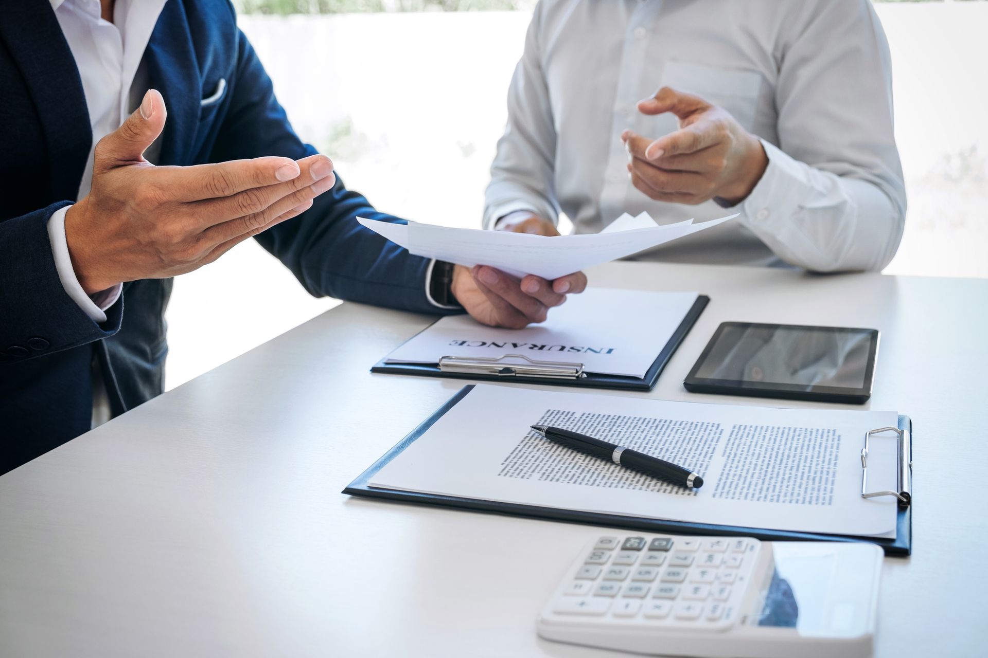 Business meeting reviewing insurance documents with tablet and calculator on desk.