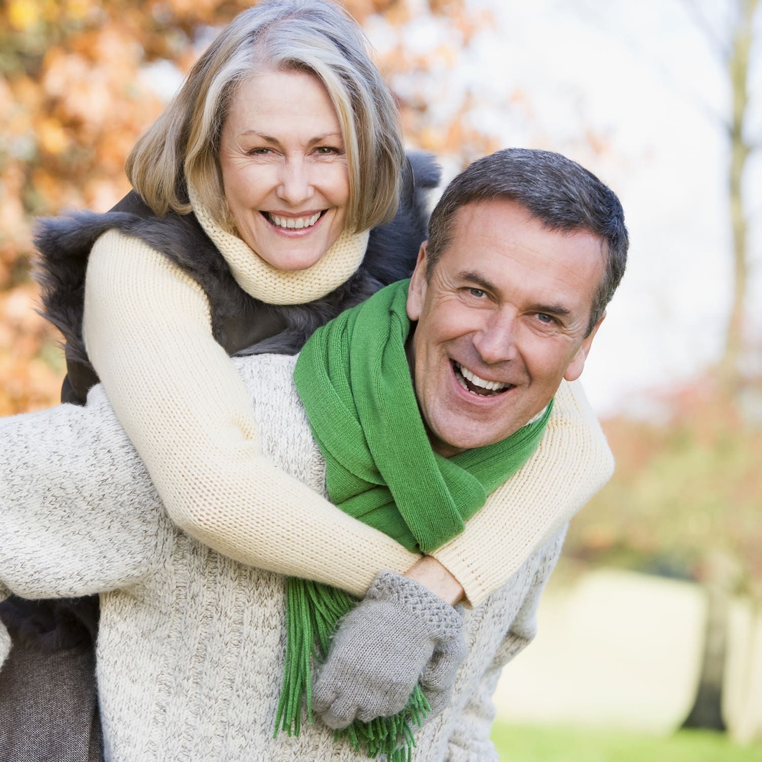 Man giving woman a piggyback ride outdoors, both smiling, fall setting.