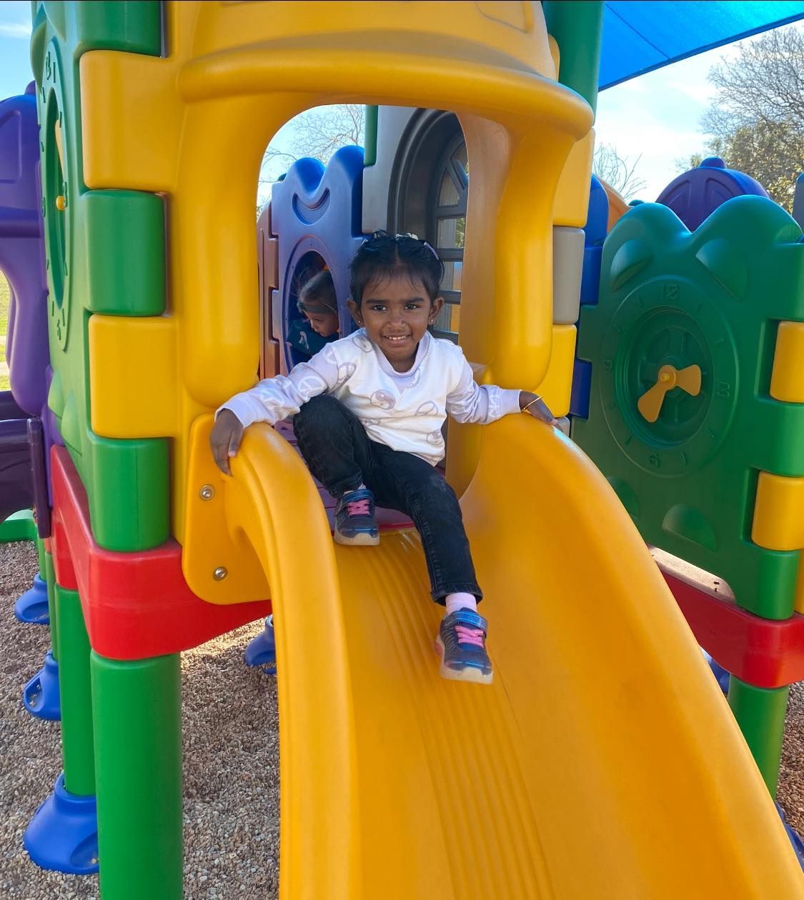 a little girl is sitting on a yellow slide in a playground