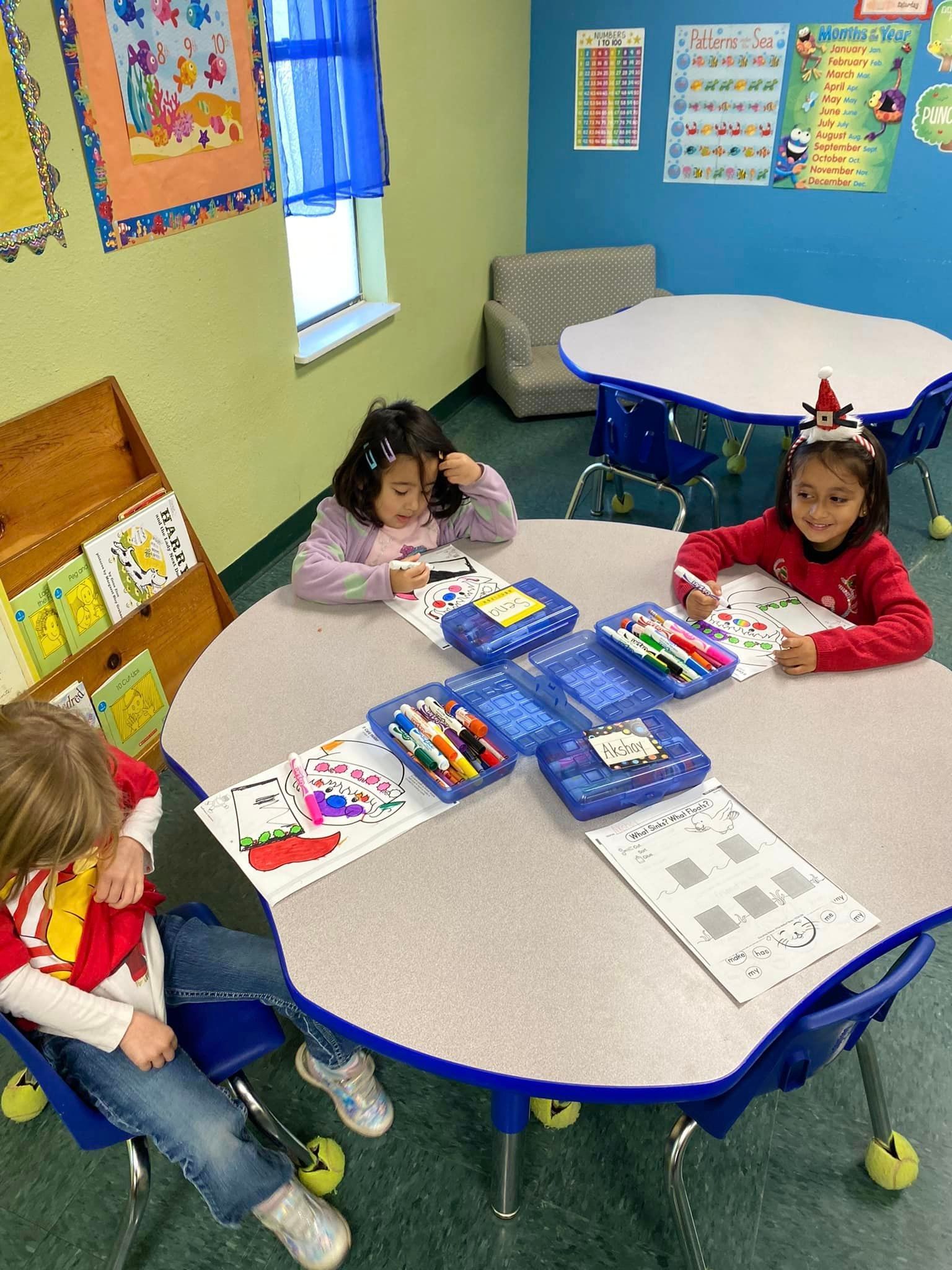 three children are sitting at a round table in a classroom