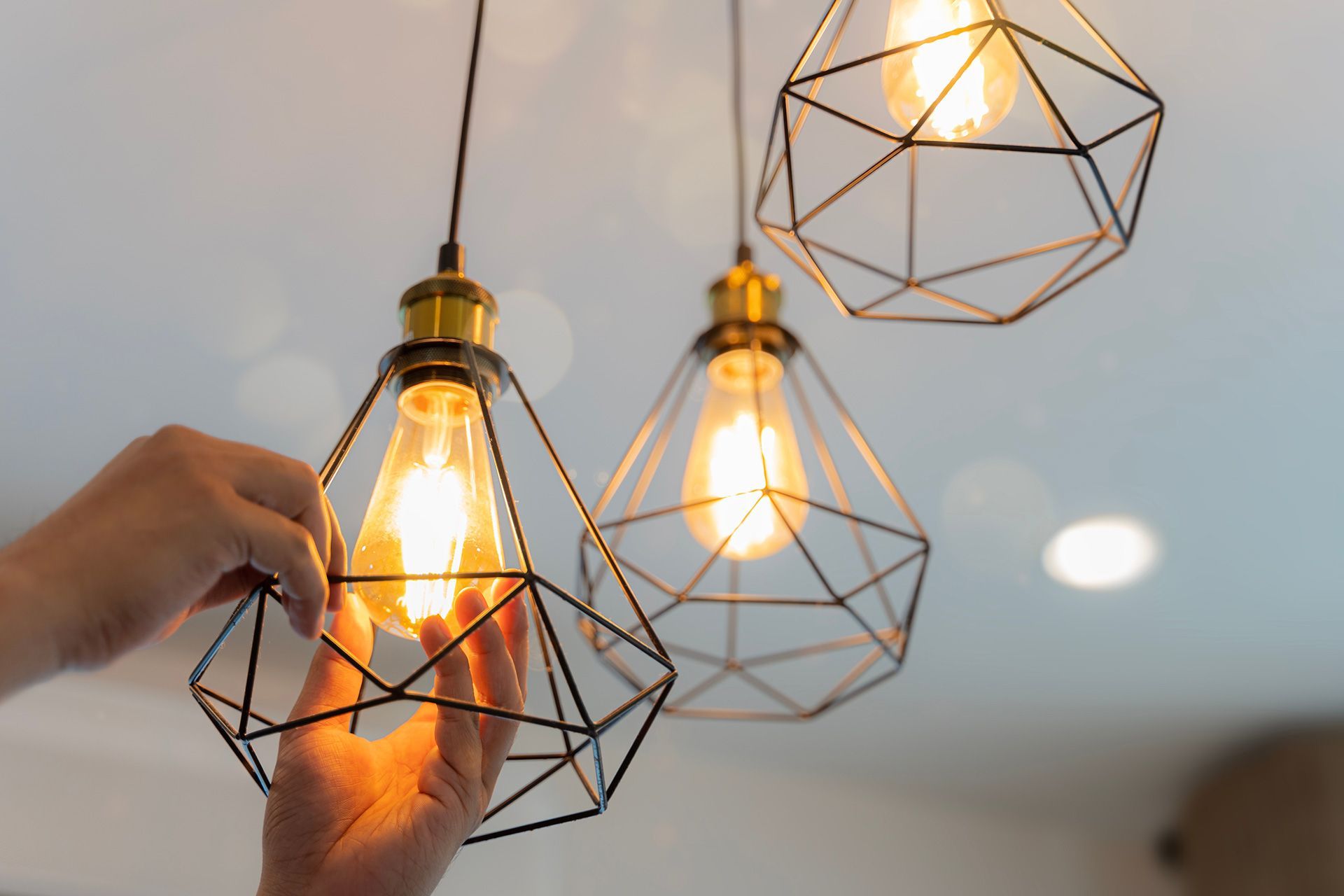 Person adjusting a geometric pendant light with an exposed lightbulb.
