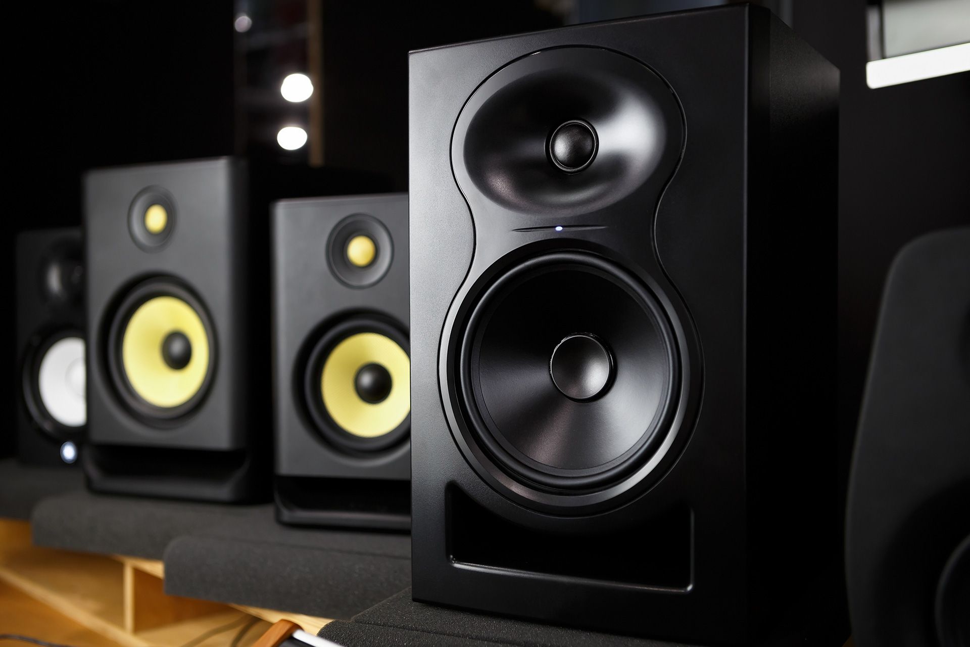 Black studio speakers with yellow and black cones, sitting on a shelf.