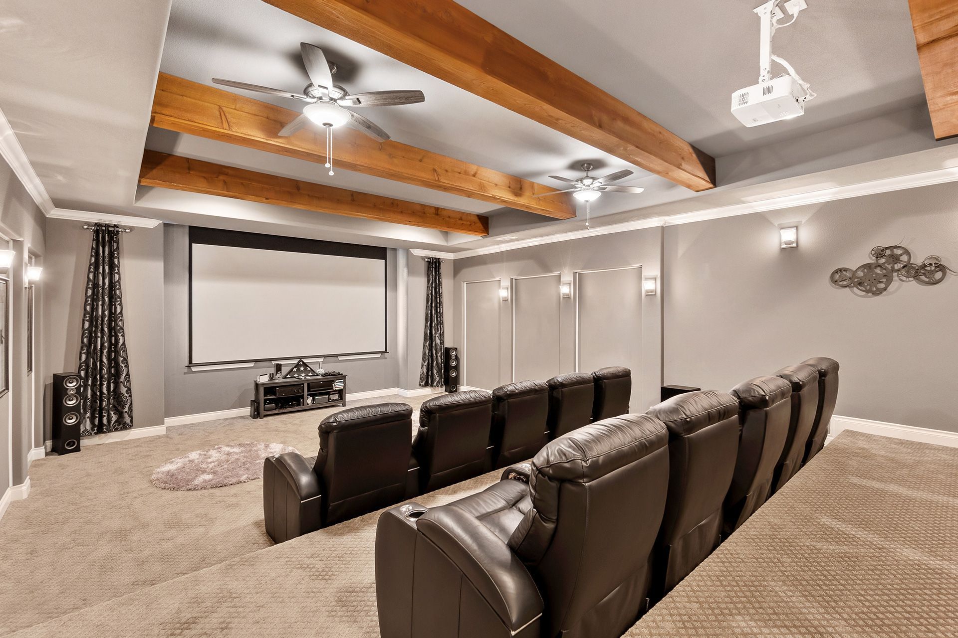 Home theater with gray walls, plush seating, projector screen, and wooden ceiling beams.