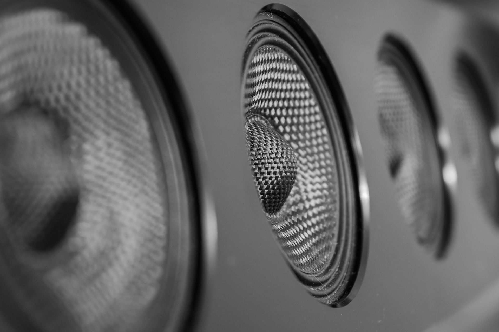 Black and white close-up of a row of audio speakers, focusing on the textured cones and metal frames.