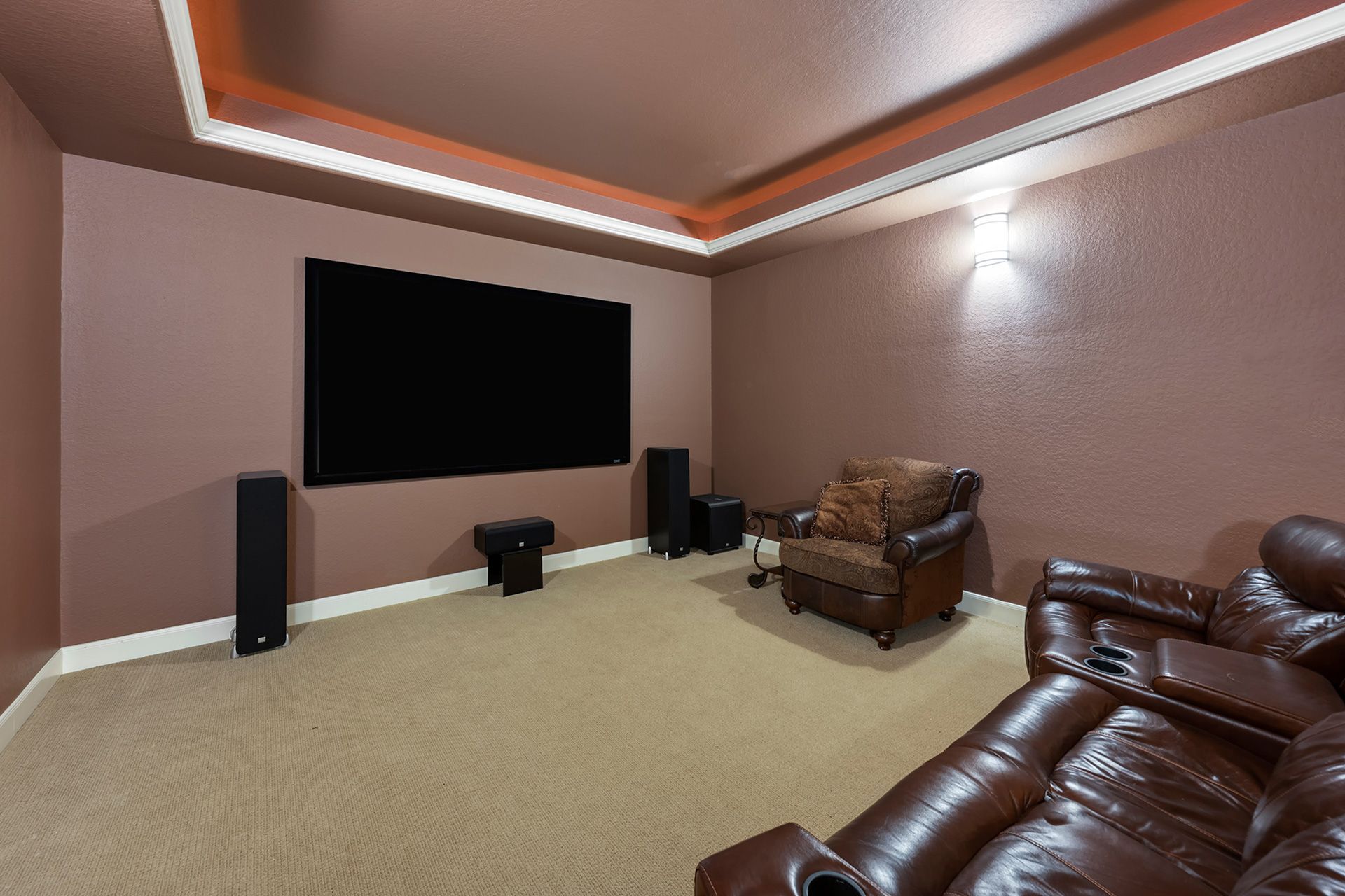 Home theater with a large black screen, brown walls, and leather seating.