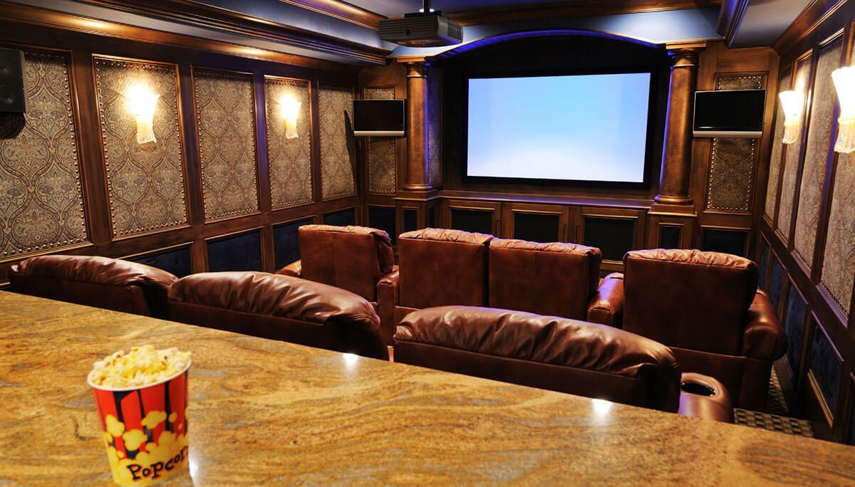 Home theater with brown leather recliners, screen, popcorn, and gold-trimmed decor.