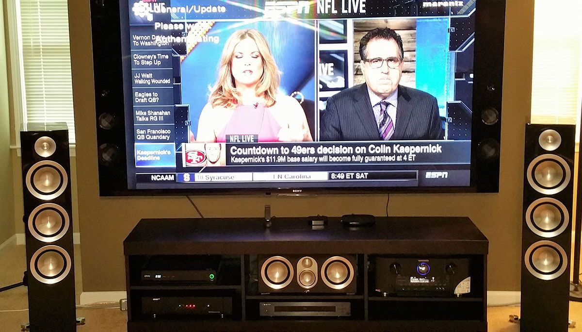 Large TV with news anchors, flanked by tall speakers, on a dark media console.