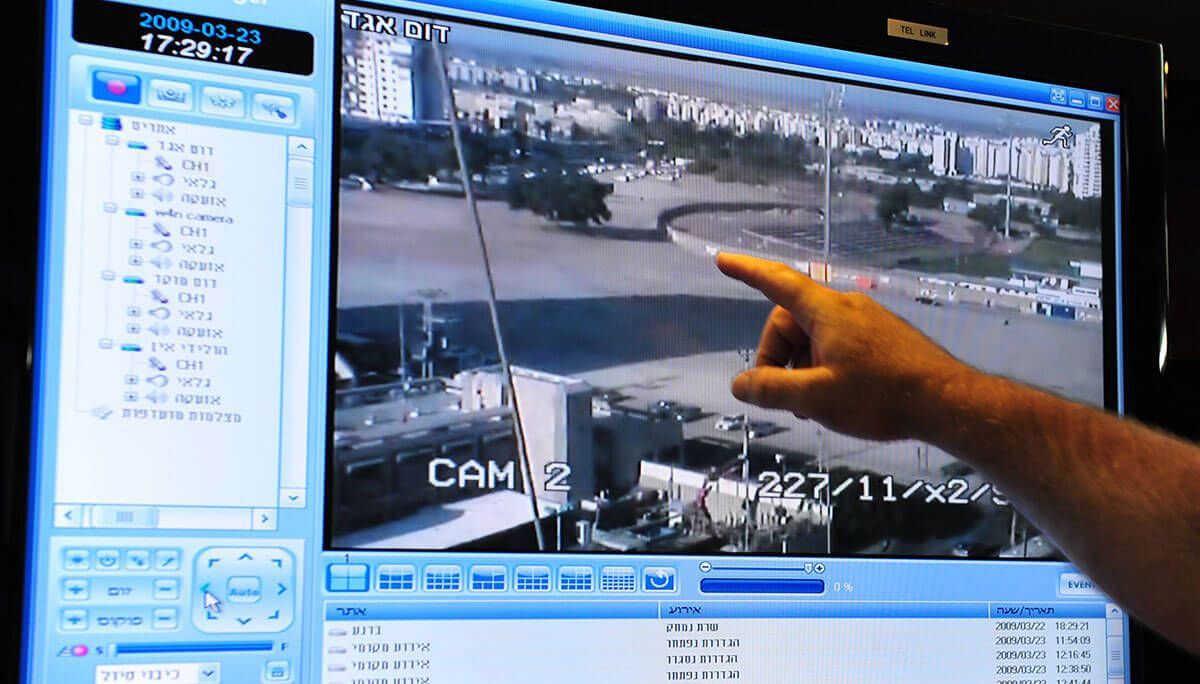 Silver intercom panel with a keypad and screen on a dark gray wall, near glass.