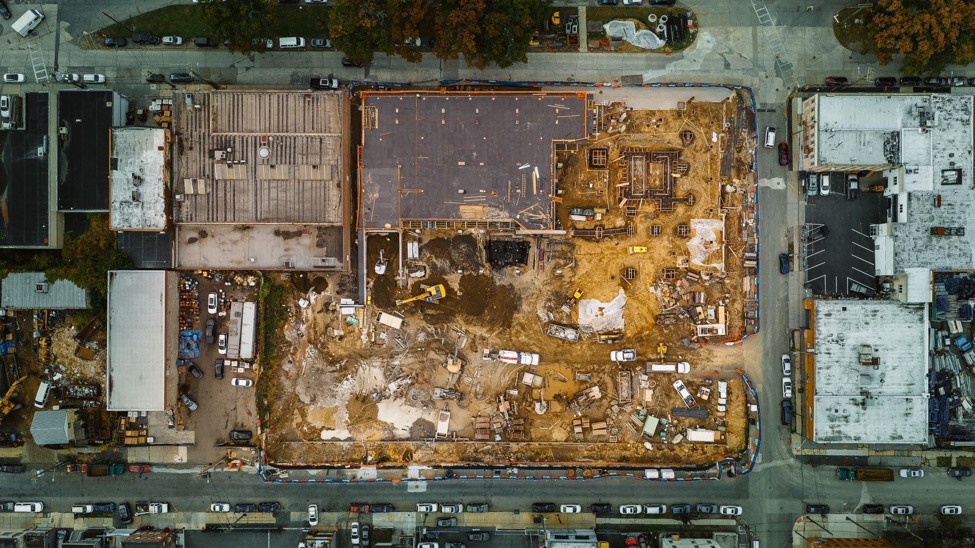 Aerial view of a demolition site between streets, with remnants of buildings, equipment, and construction materials visible.
