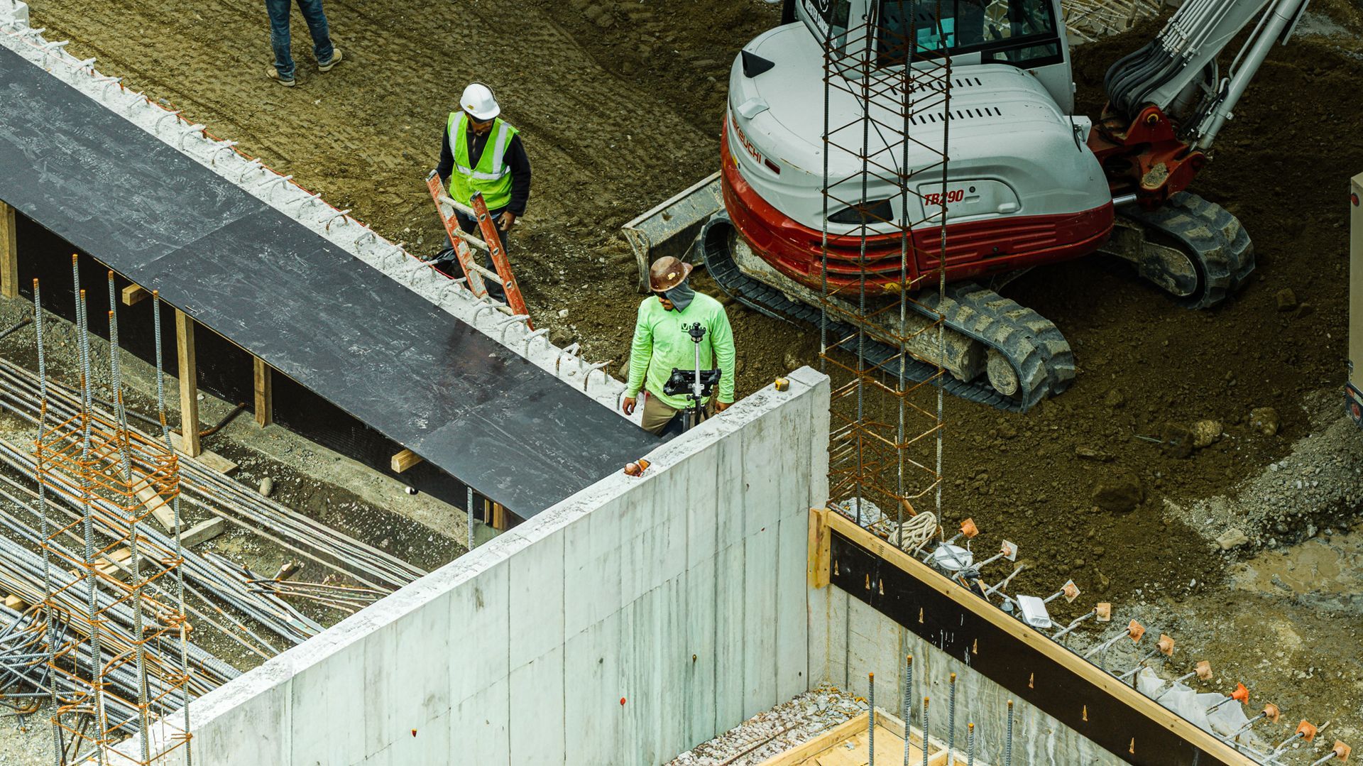 Construction site with workers, excavator, and concrete walls.