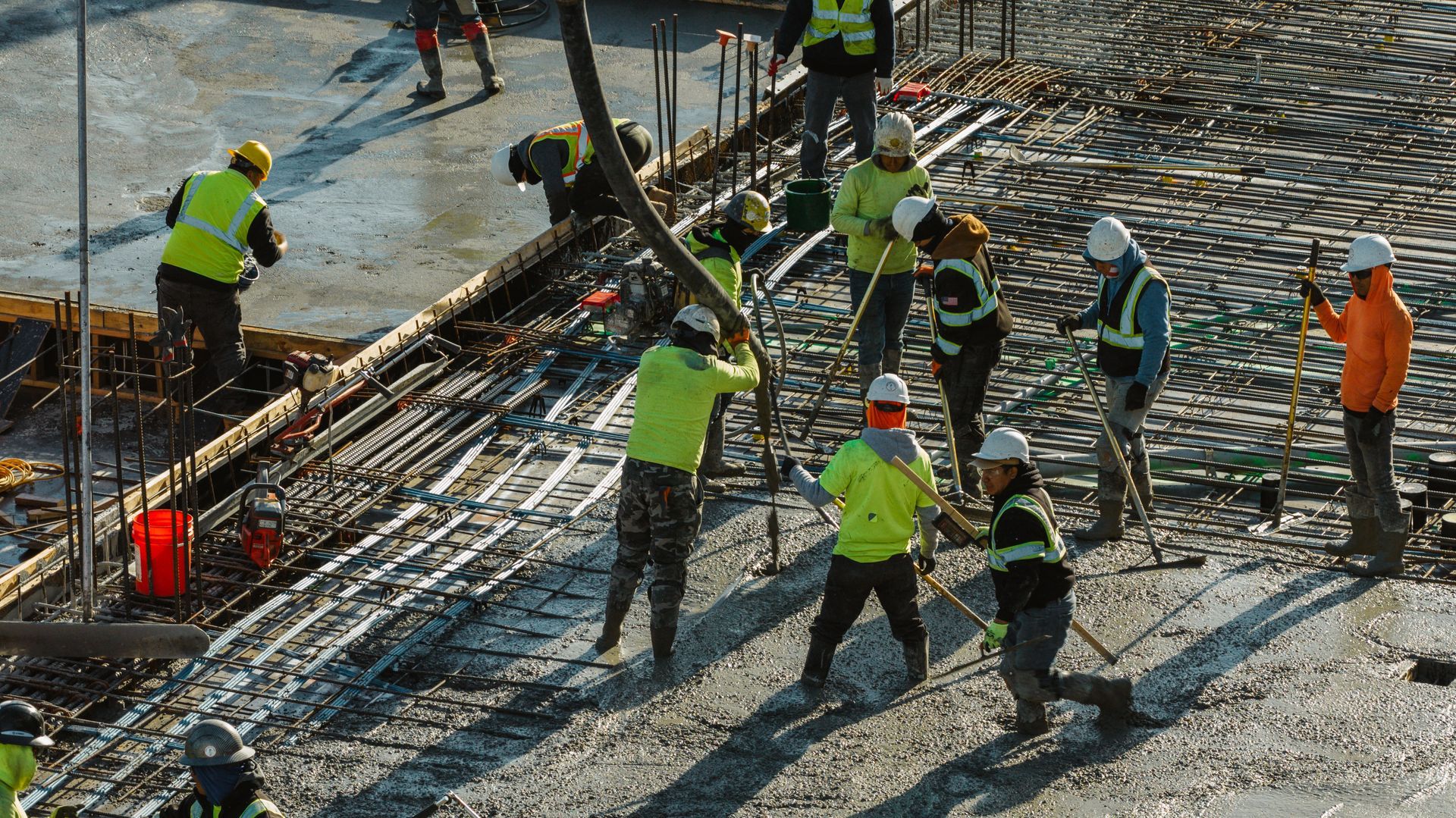 Construction workers pouring concrete on a building site. Workers wear safety vests and helmets.