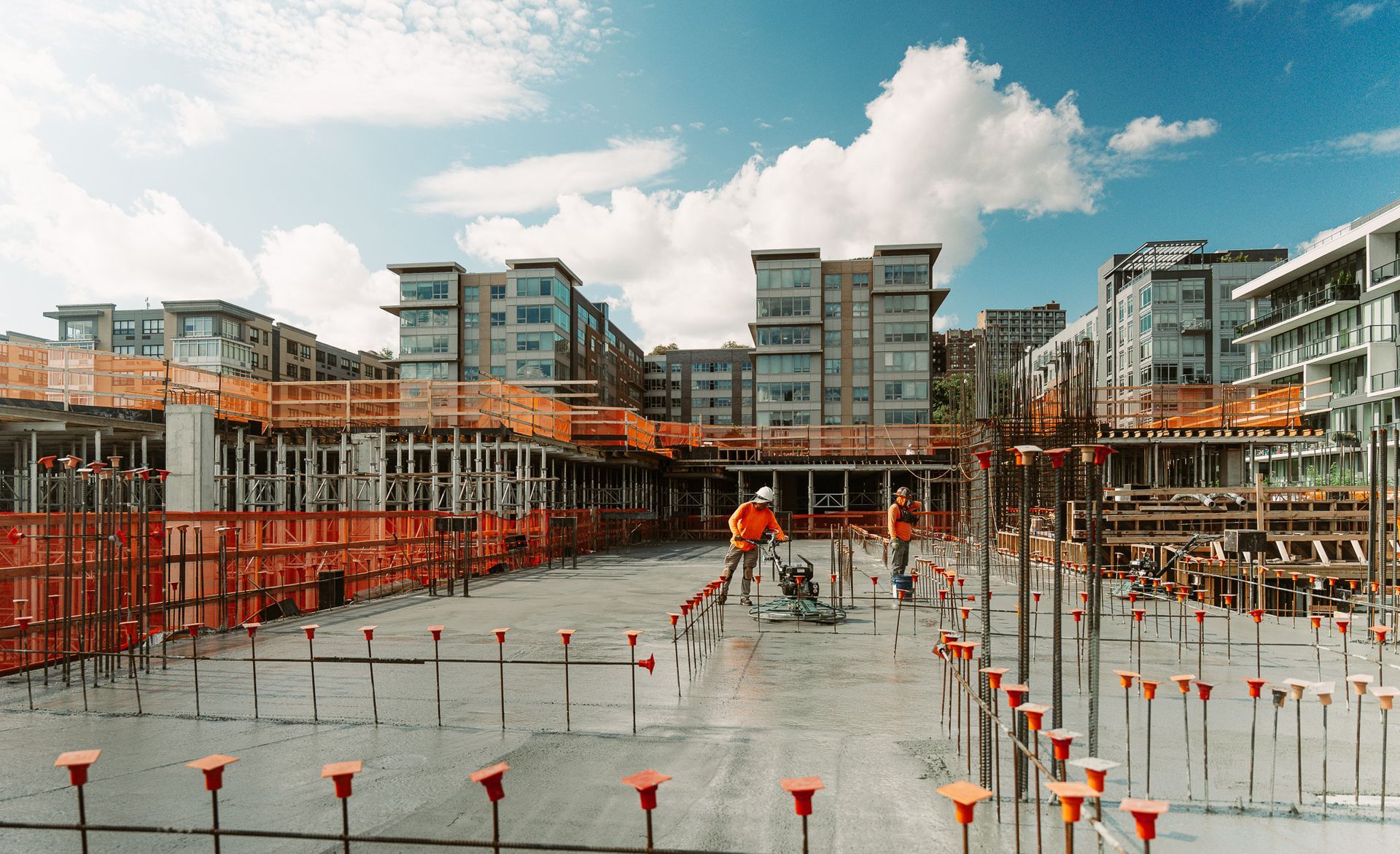 Construction site with workers, concrete, and buildings under construction on a sunny day.