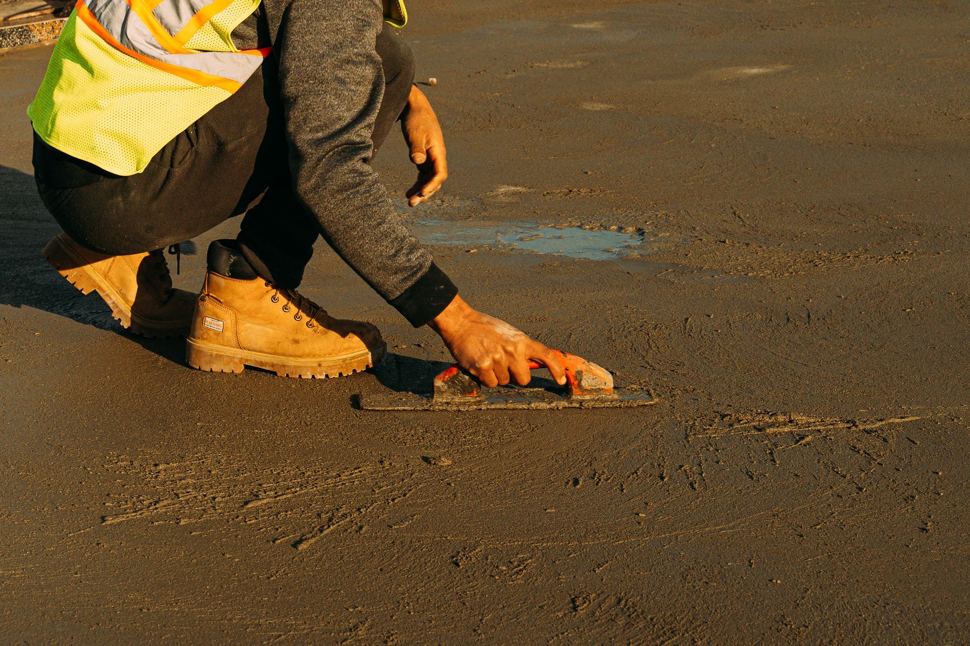 Person in work boots and vest smoothing asphalt with a trowel.