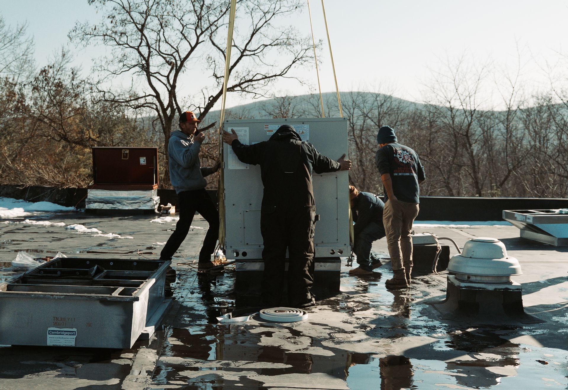 Workers install HVAC unit on rooftop in winter.