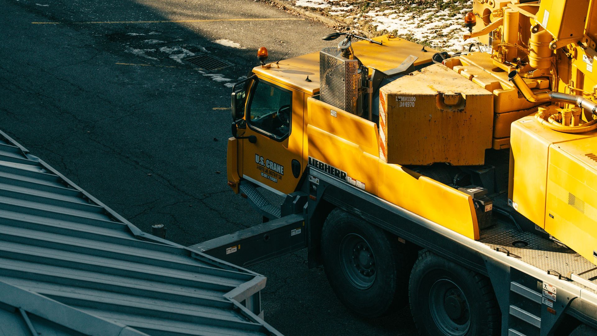 Yellow crane truck parked on asphalt; sunlight.