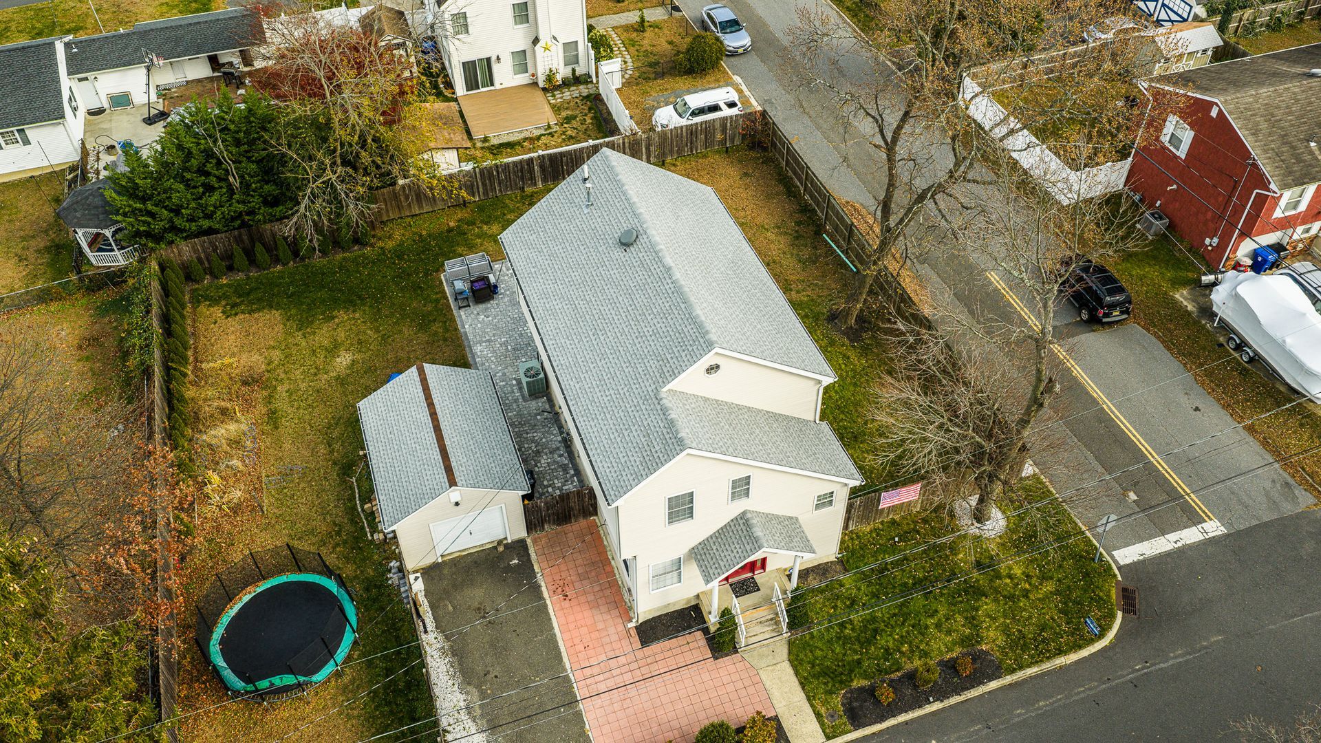 Aerial view of a two-story beige house with a gray roof and attached garage, next to a street with cars and other houses.
