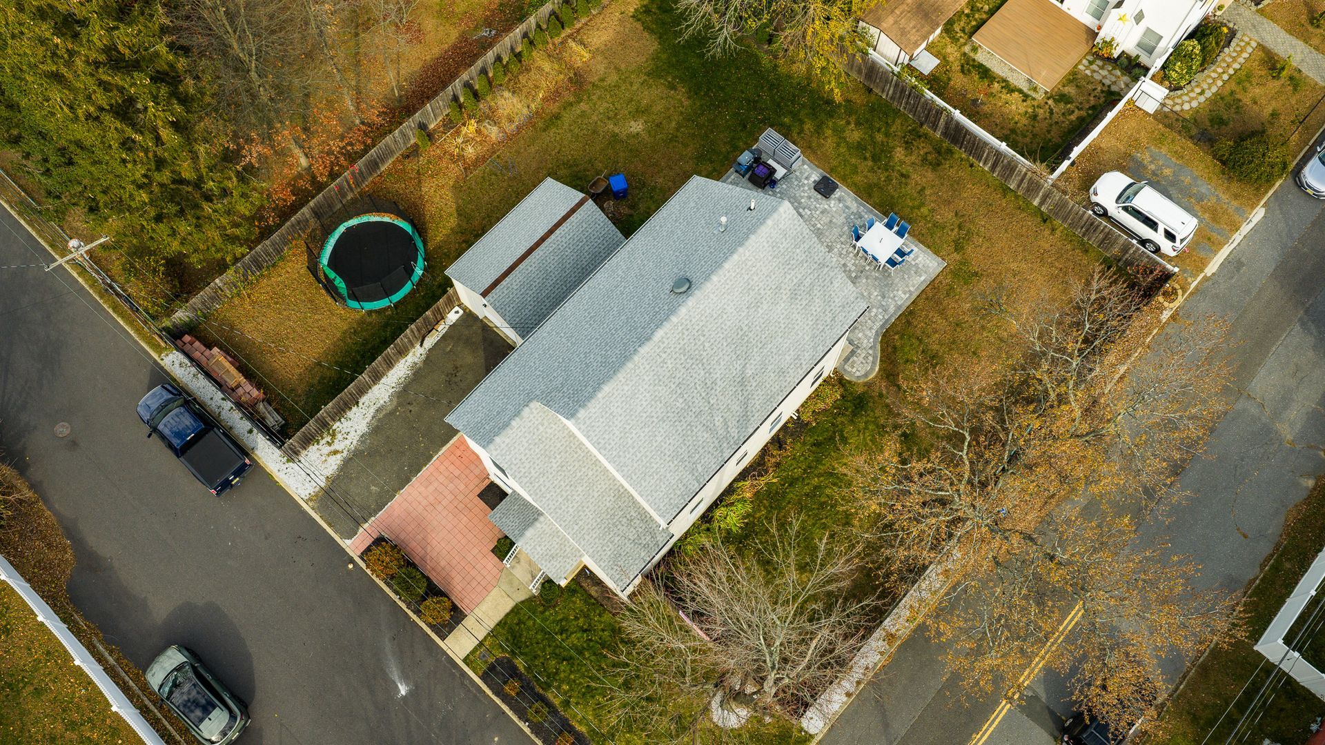 Aerial view of a house at a street intersection, with a small yard, shed, and cars on the street.