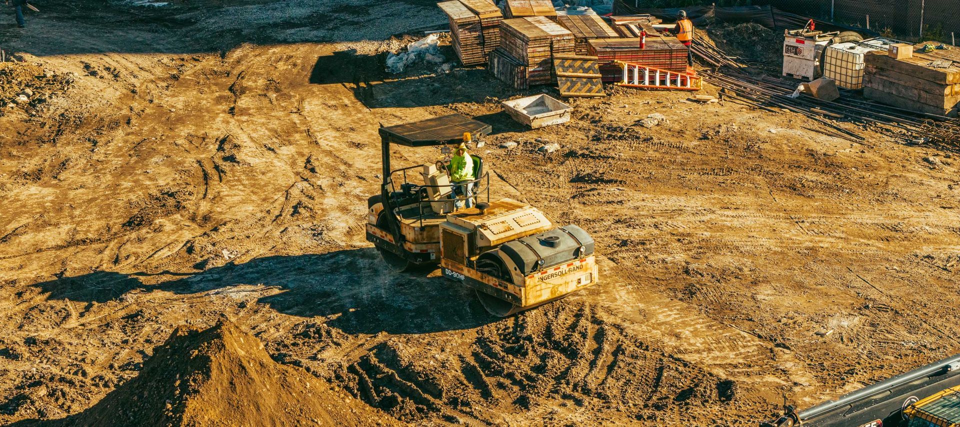 A yellow soil compactor at a construction site, with dirt and building materials.