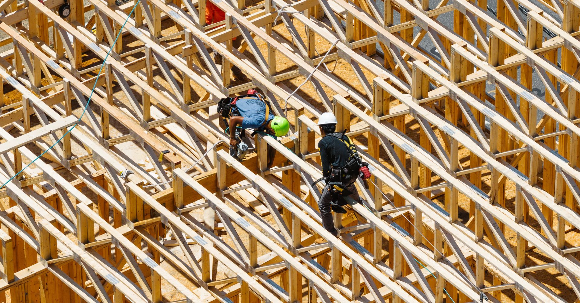 Workers on wooden roof frame, wearing safety harnesses and helmets.