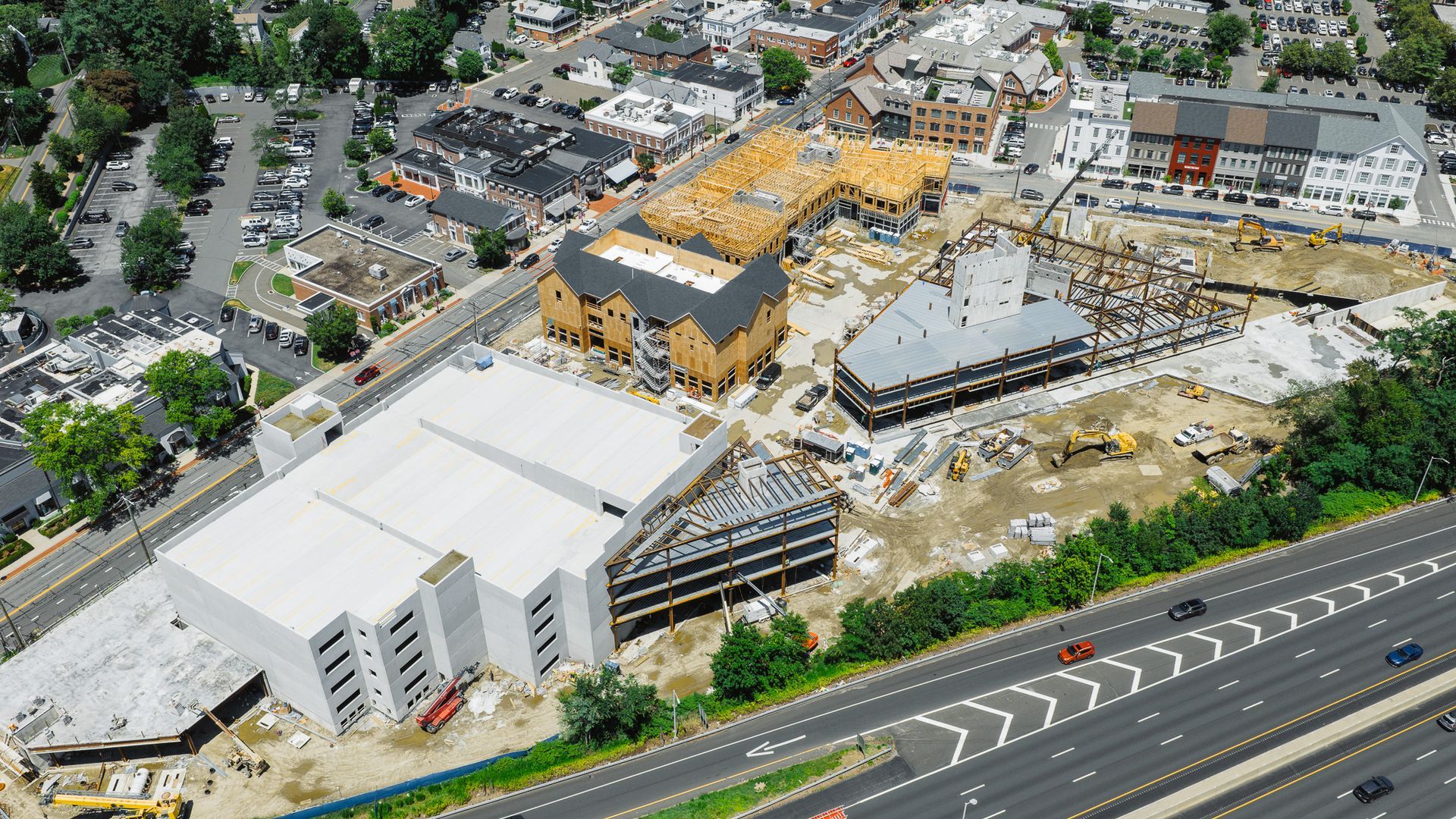 Aerial view of a construction site with several buildings under construction near a highway and residential area.