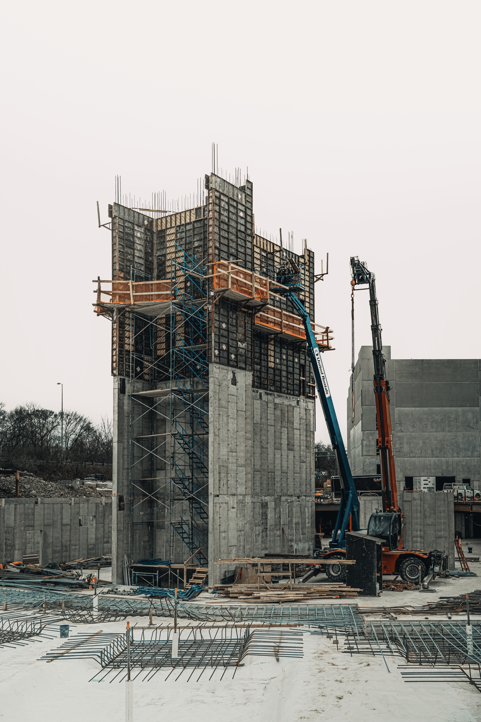 Construction site with a tall concrete structure, crane, and various building materials. Overcast sky.