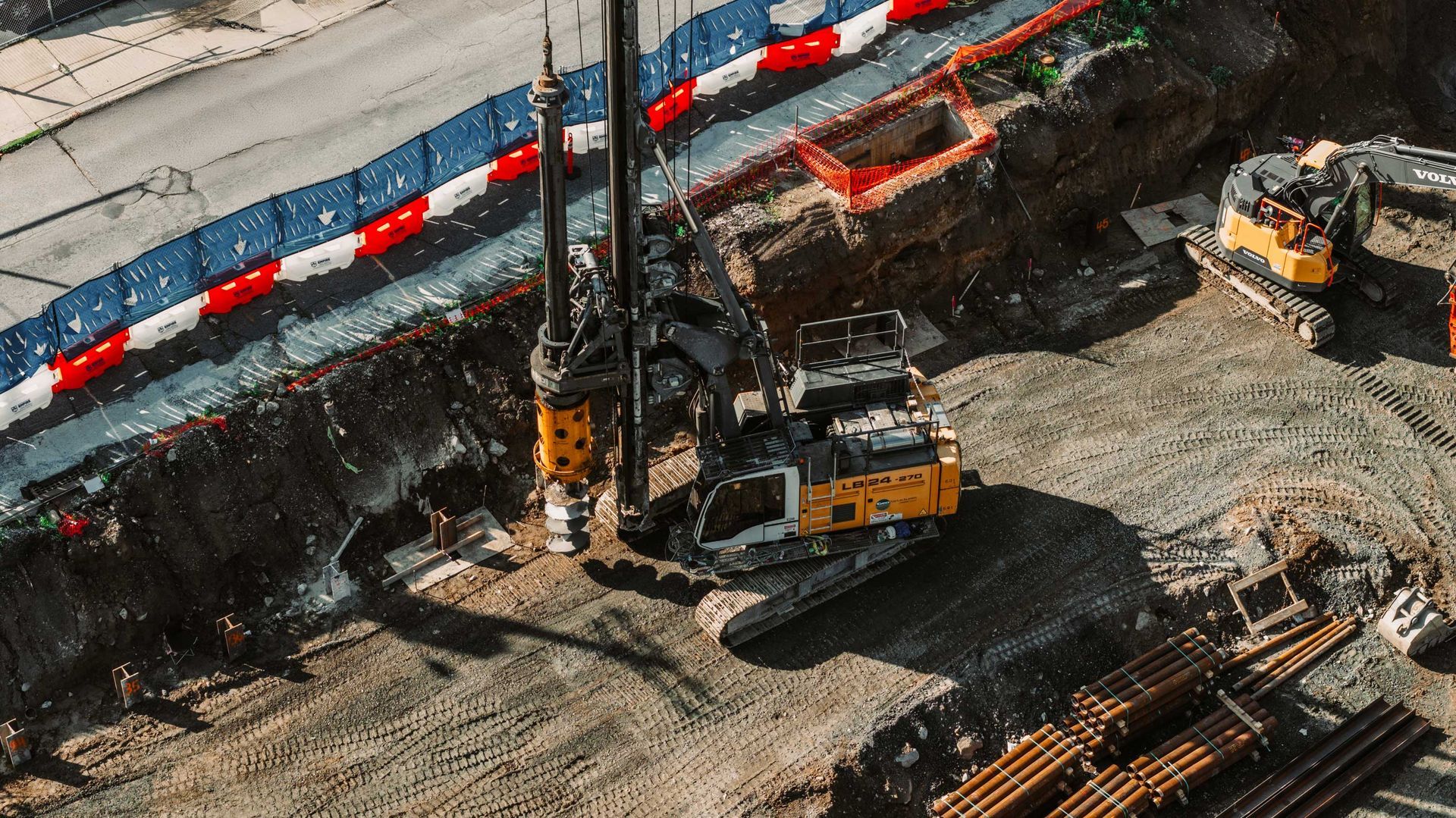 Construction site with heavy machinery, including a drilling machine, digging in a trench.