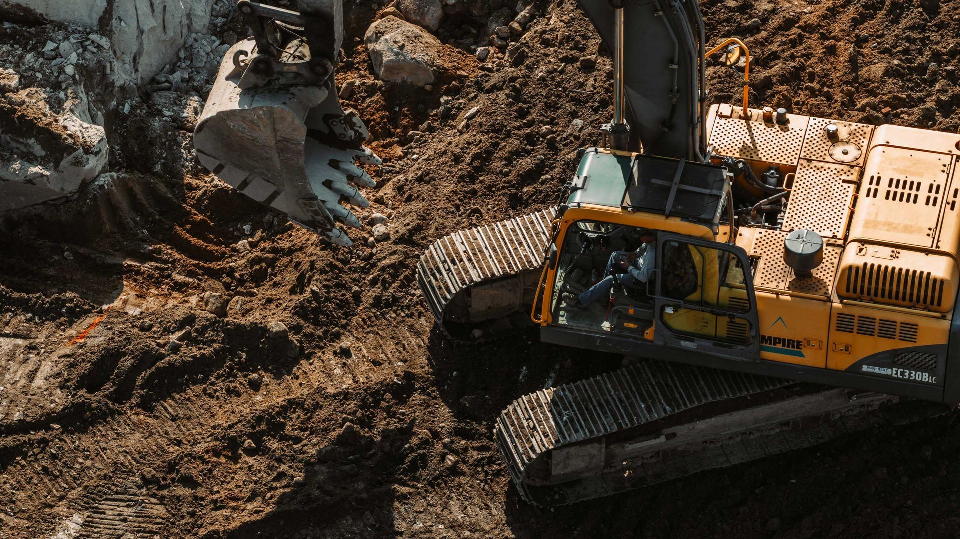 Yellow excavator digging into brown soil and rocks.