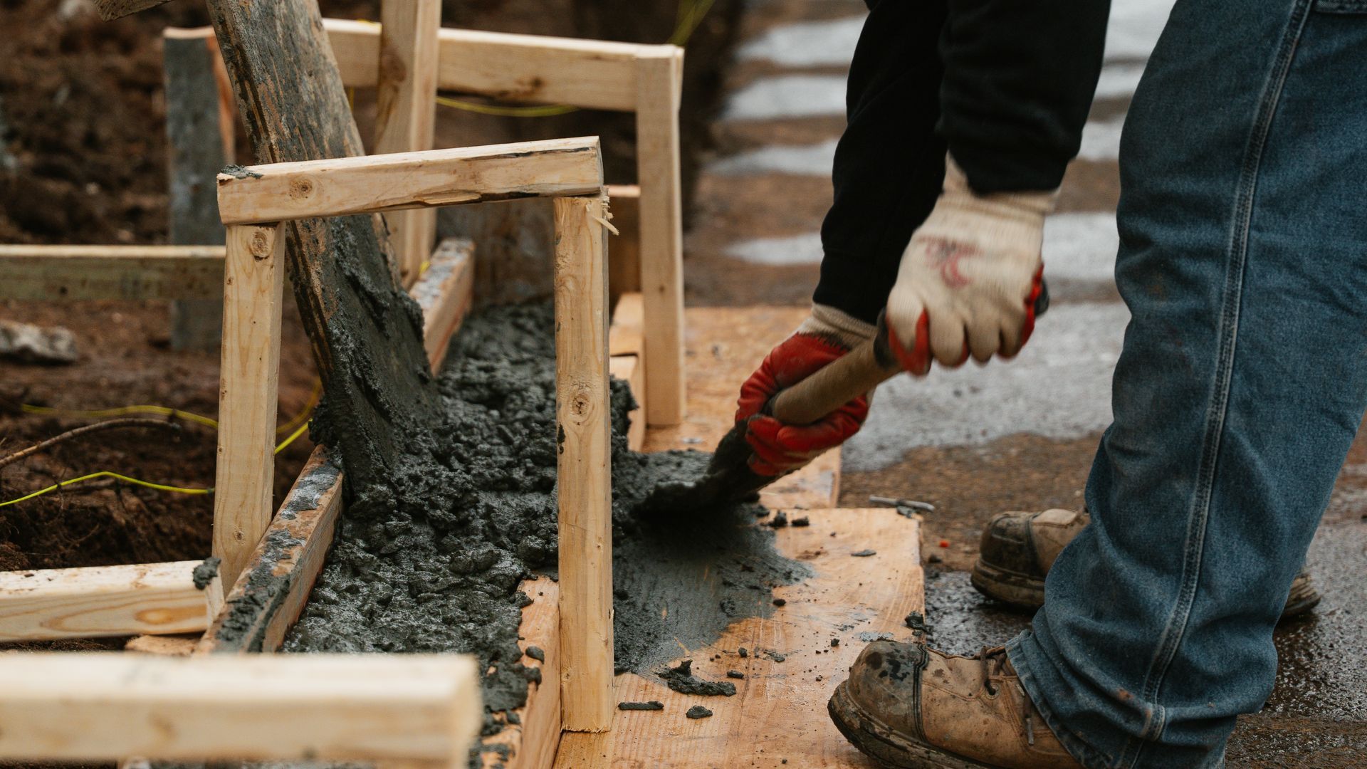 Person pouring concrete into wooden formwork with a shovel.
