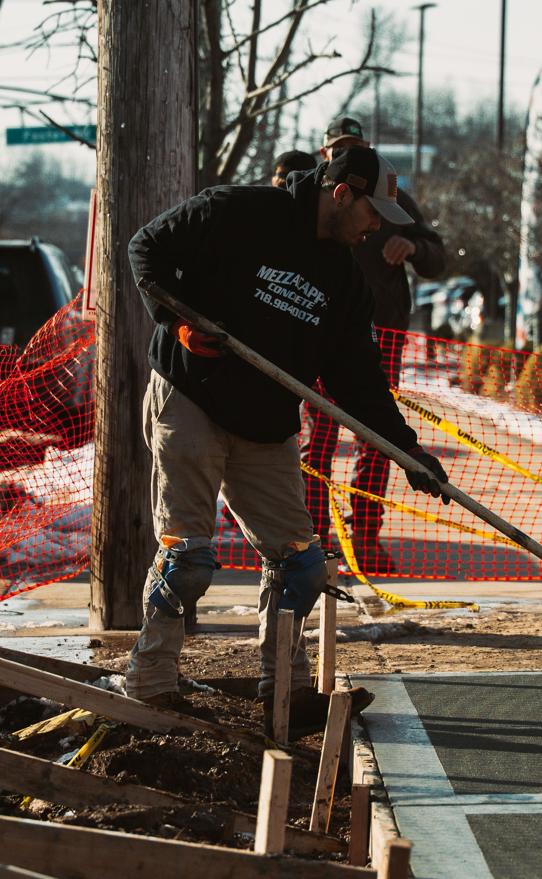 Construction worker using a shovel at a construction site near a road and power pole.