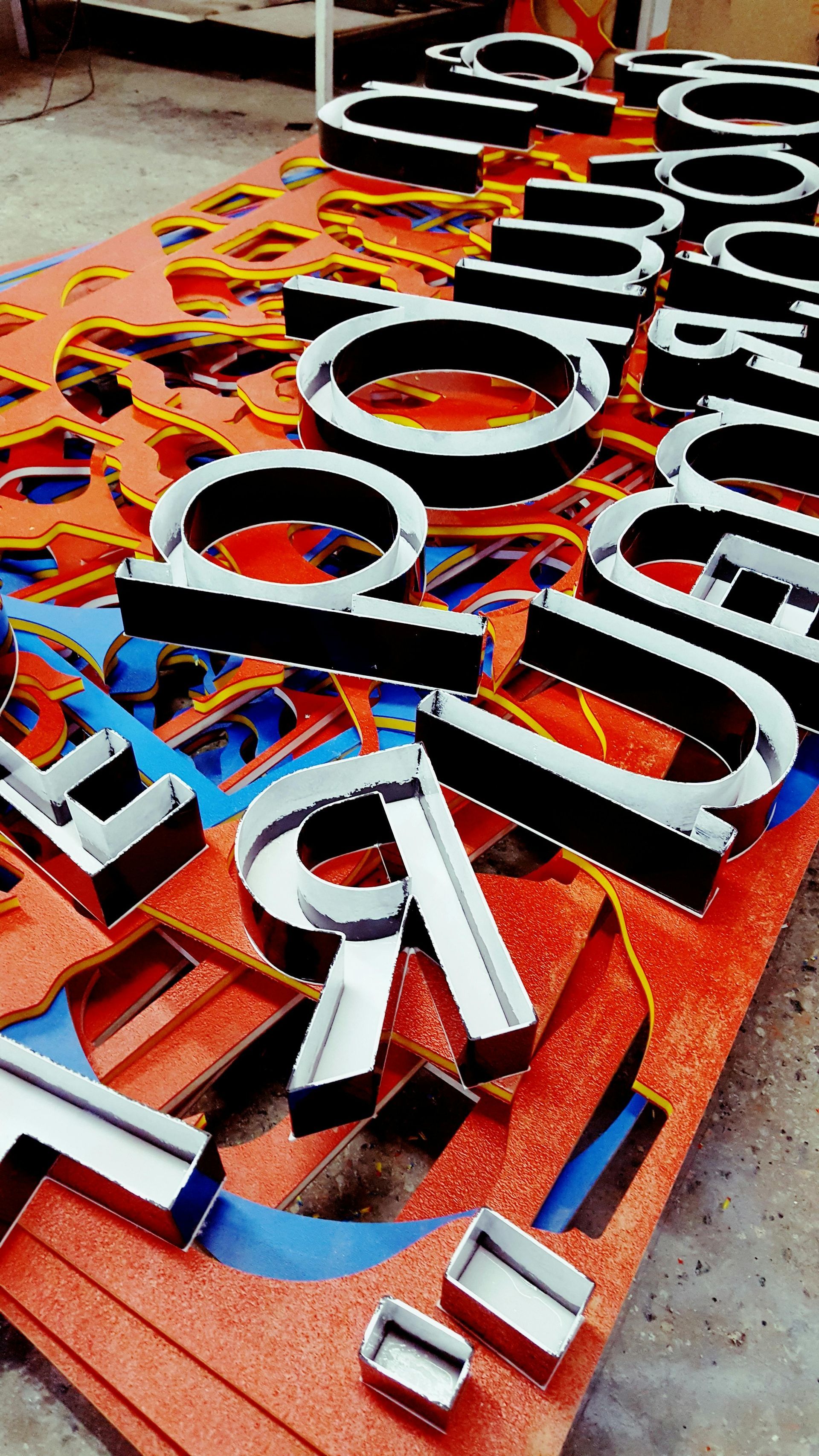 Metal channel letters arranged on a colorful, patterned surface, likely for a sign.
