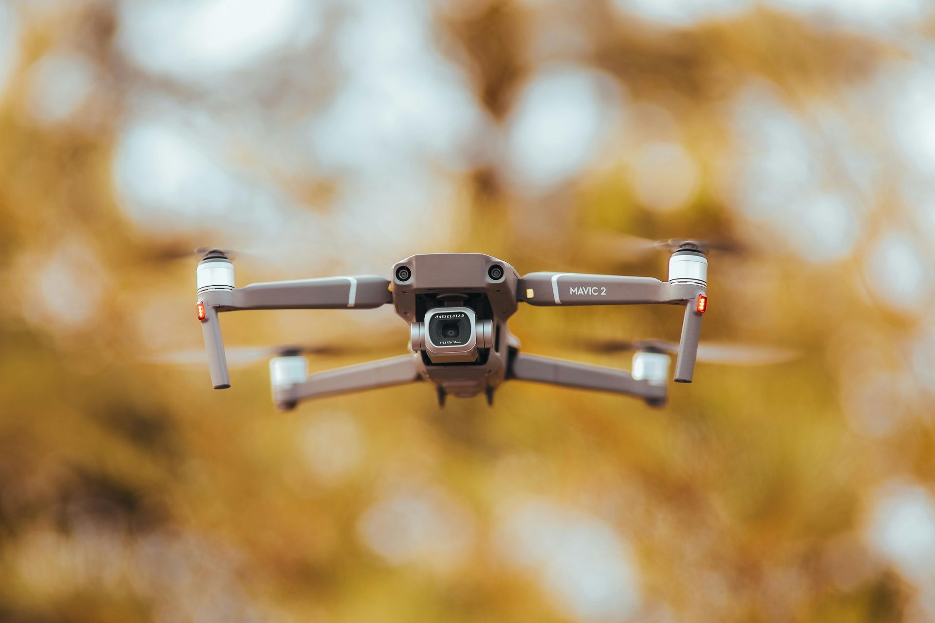 Drone in flight over a rocky coastline at sunset; orange sky, ocean waves.