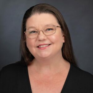 A woman wearing glasses and a black shirt is smiling for the camera.