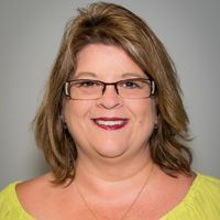 A woman wearing glasses and a yellow shirt is smiling for the camera.