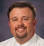 A man with a beard is smiling for the camera while wearing a white shirt and tie.