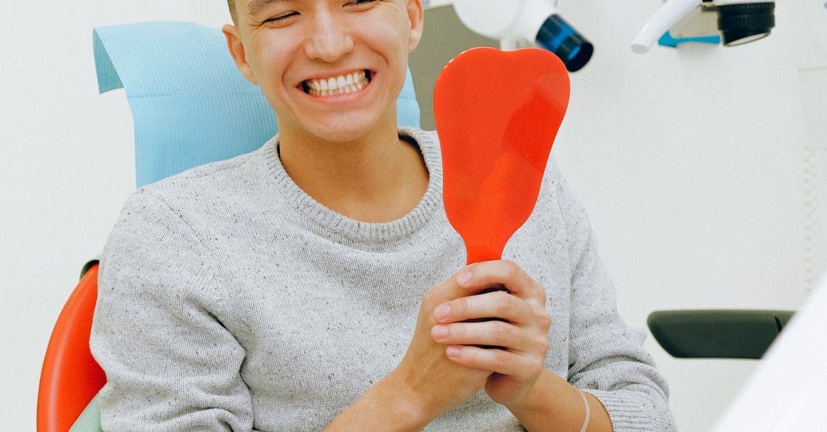 A man is sitting in a dental chair holding a red heart shaped mirror.