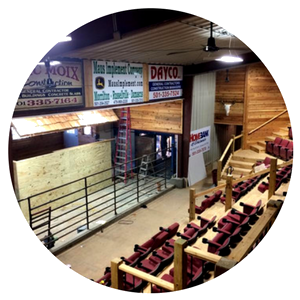 An indoor arena featuring tiered rows of red theater-style seats facing a wooden stage and metal barricades.