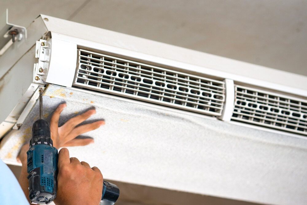 A Man Is Using A Drill To Fix An Air Conditioner — Bear Air Conditioning In The Entrance, NSW