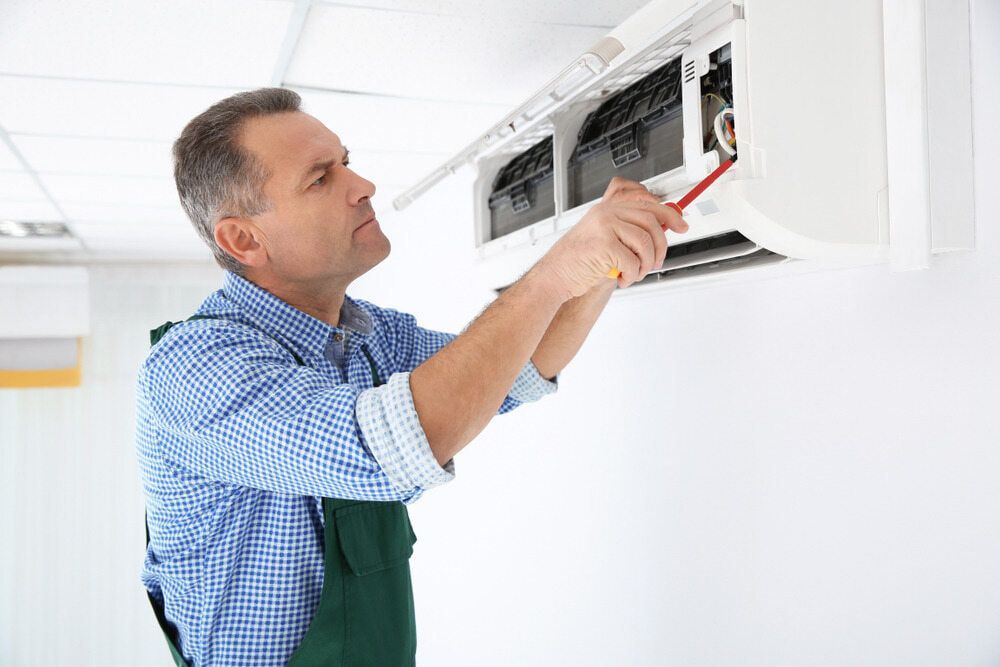 A Man Is Fixing An Air Conditioner With A Screwdriver — Bear Air Conditioning In Hamlyn Terrace, NSW