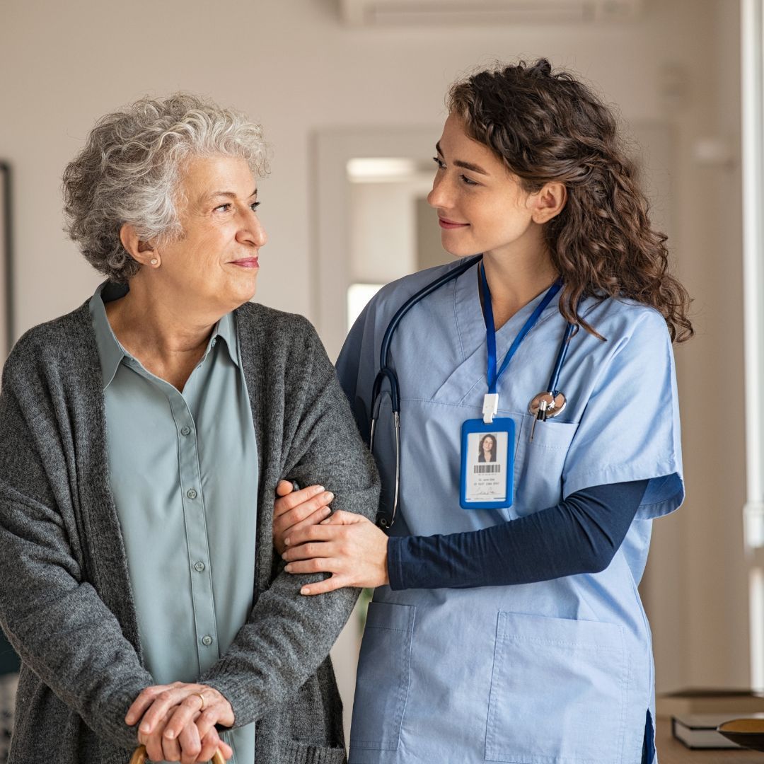 A nurse is standing next to an older woman with a cane.