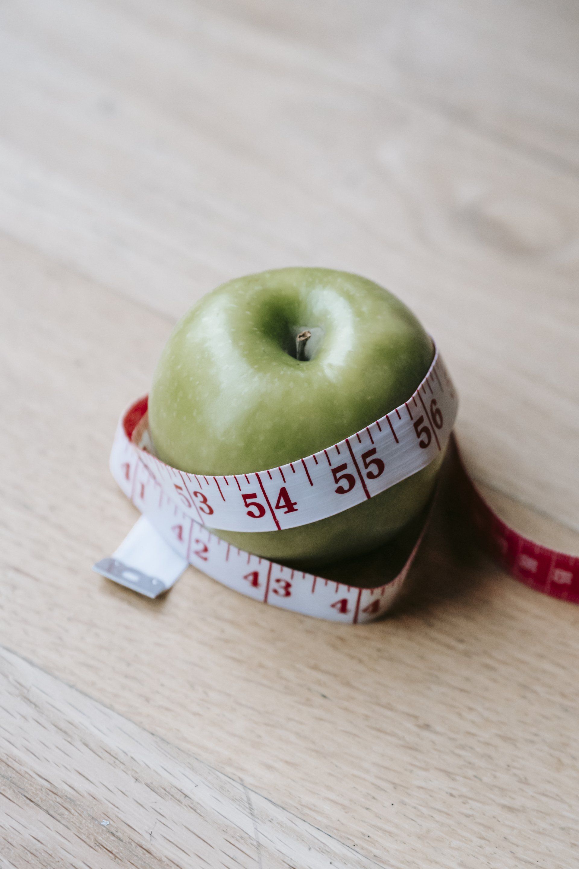 A green apple is wrapped in a measuring tape on a wooden table.