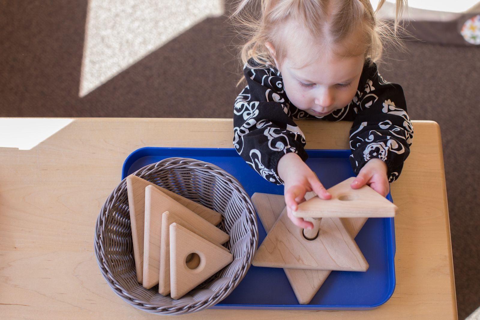 A young child with pigtails focused on completing a wooden puzzle with animal shapes at a table.