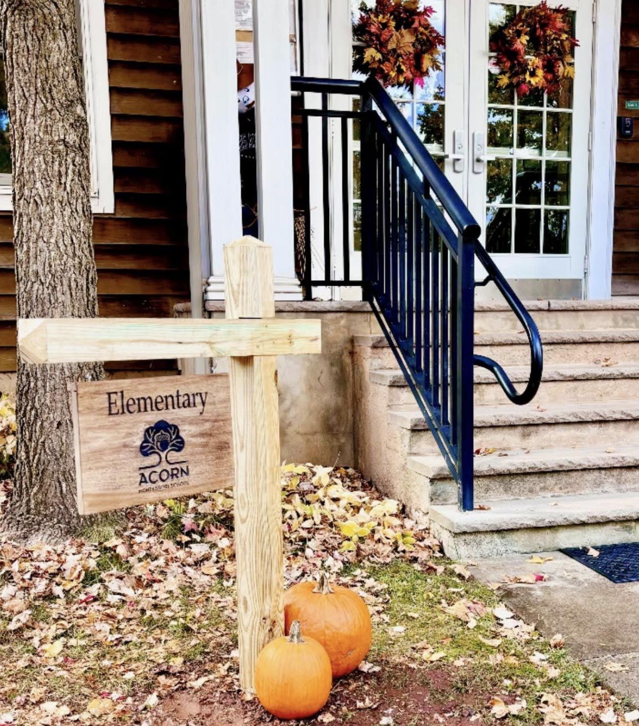 The autumn-decorated entrance of the Acorn Montessori School elementary building, featuring a wooden sign, pumpkins, and fall wreaths on the doors.